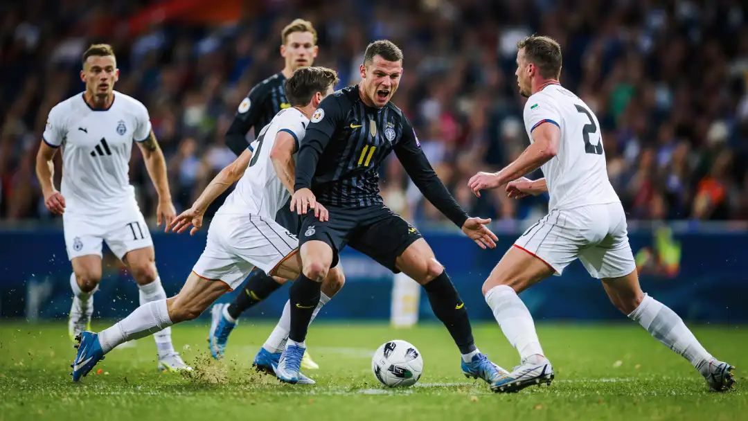 A captain shields the ball under pressure from two defenders in a tense group-of-death match