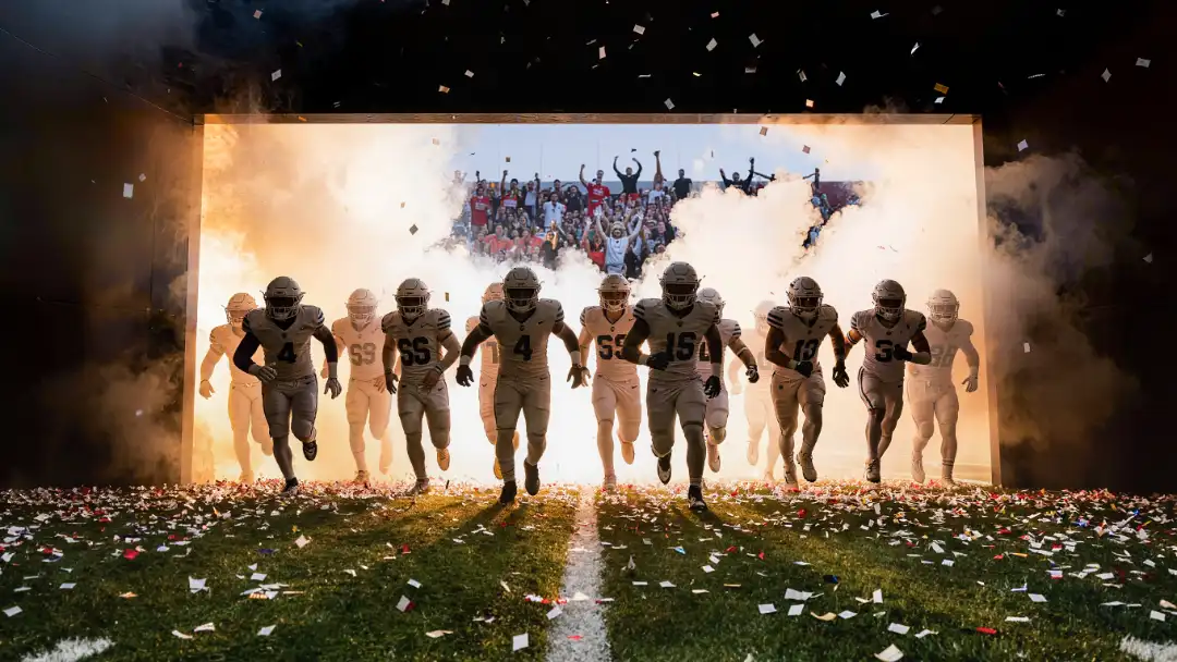 Football team running out of the tunnel through smoke into a roaring stadium