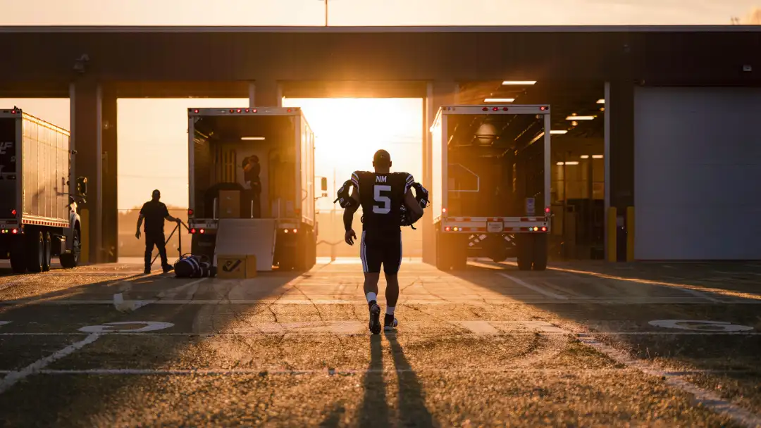 Player carrying shoulder pads toward the team facility at sunrise on day one of camp