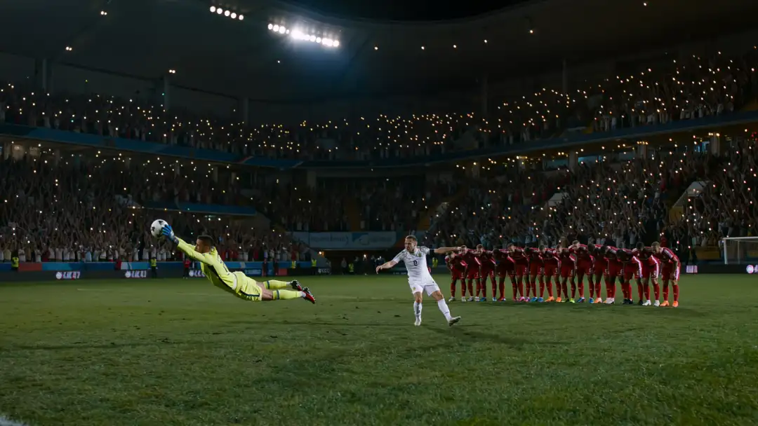 A goalkeeper dives during a penalty shootout as teammates watch from the center circle