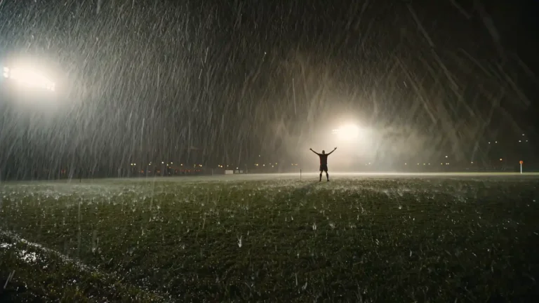 Lone player silhouette celebrating on a rain-soaked pitch under floodlights